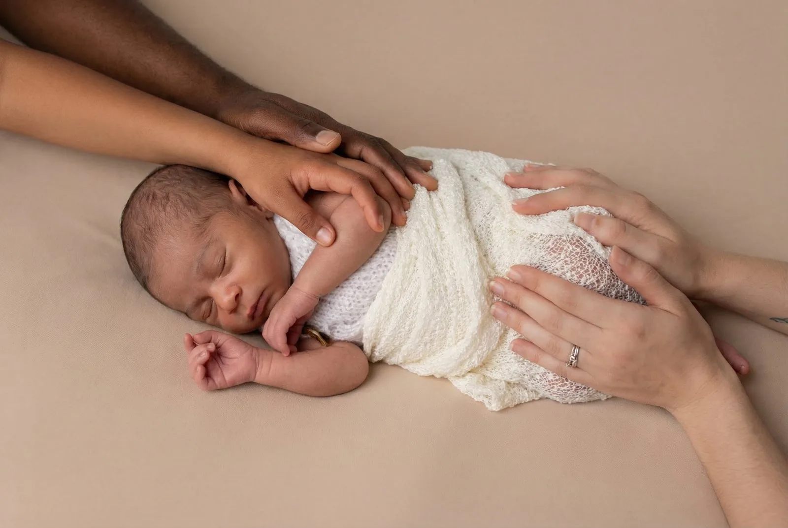 Un nouveau-né emmailloté endormi, entouré des mains de ses parents
