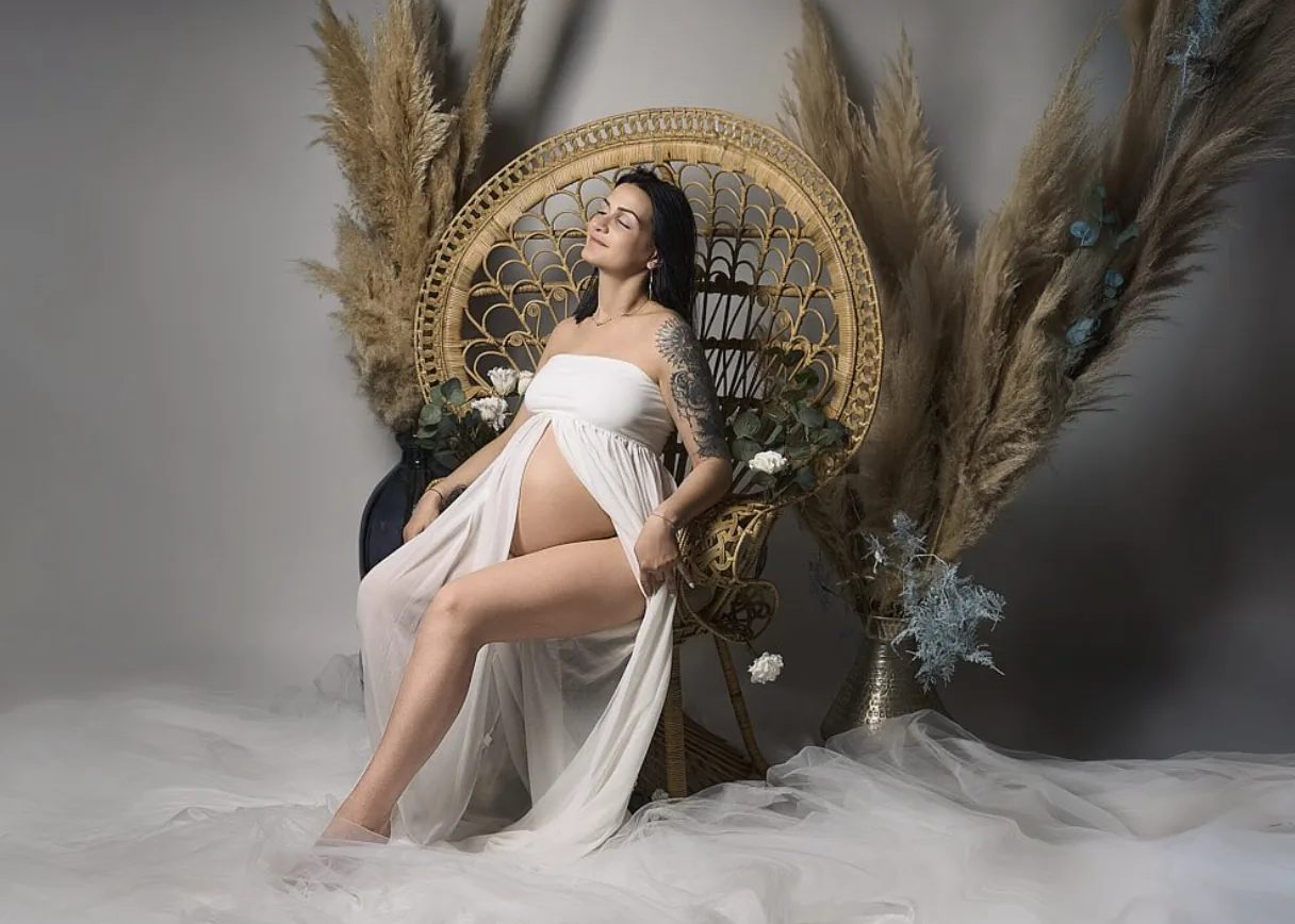 Future maman sur un fauteuil en rotin entre des herbes de pampa