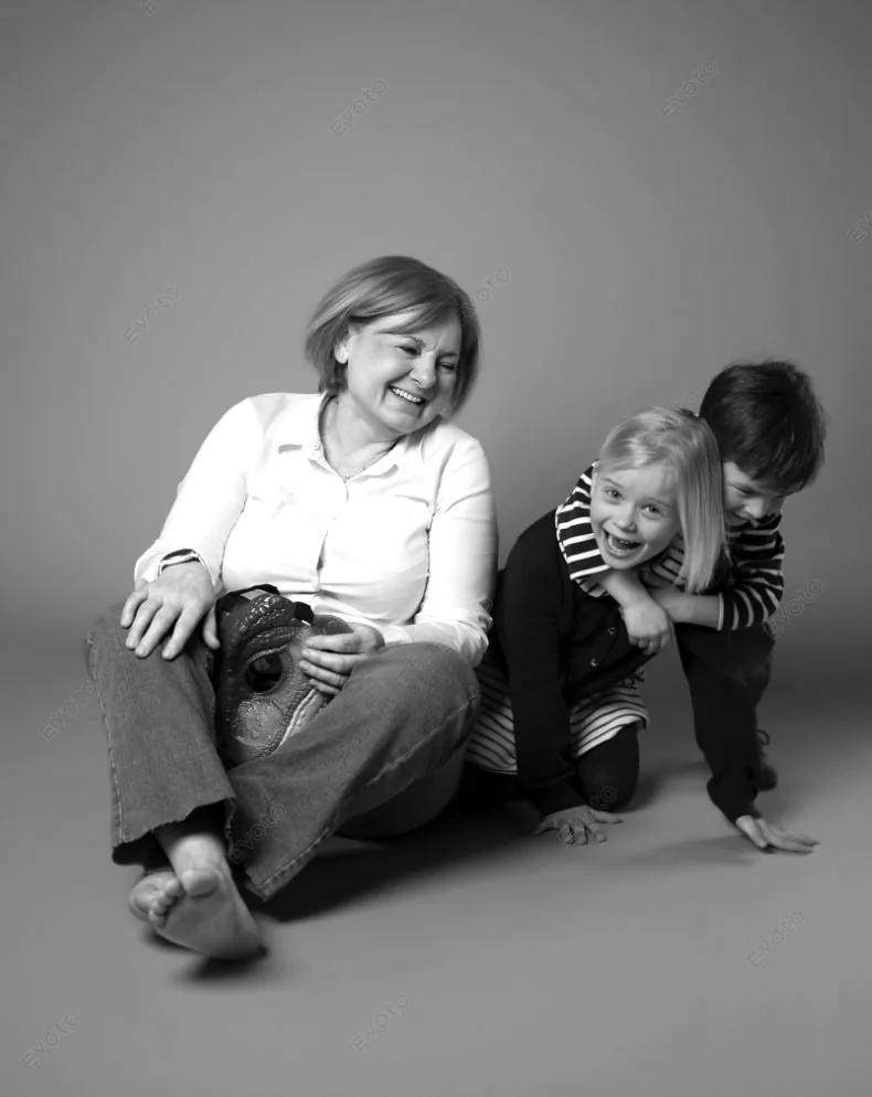 Une grand-mère rit avec ses deux petits-enfants assis au sol