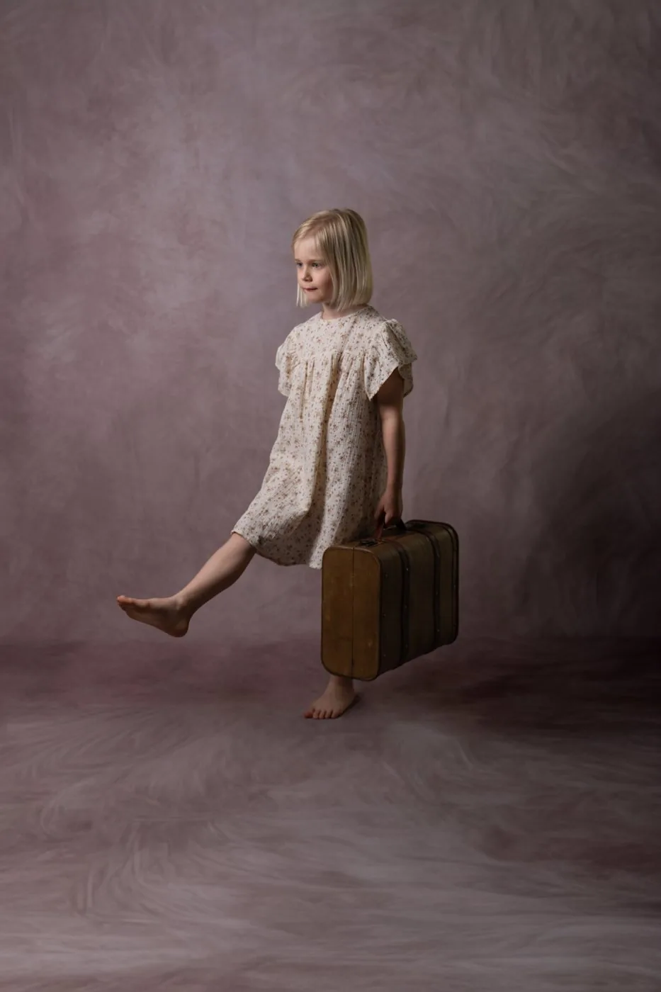 Une fillette en robe à fleurs avance d'un pas joyeux, une valise ancienne à la main