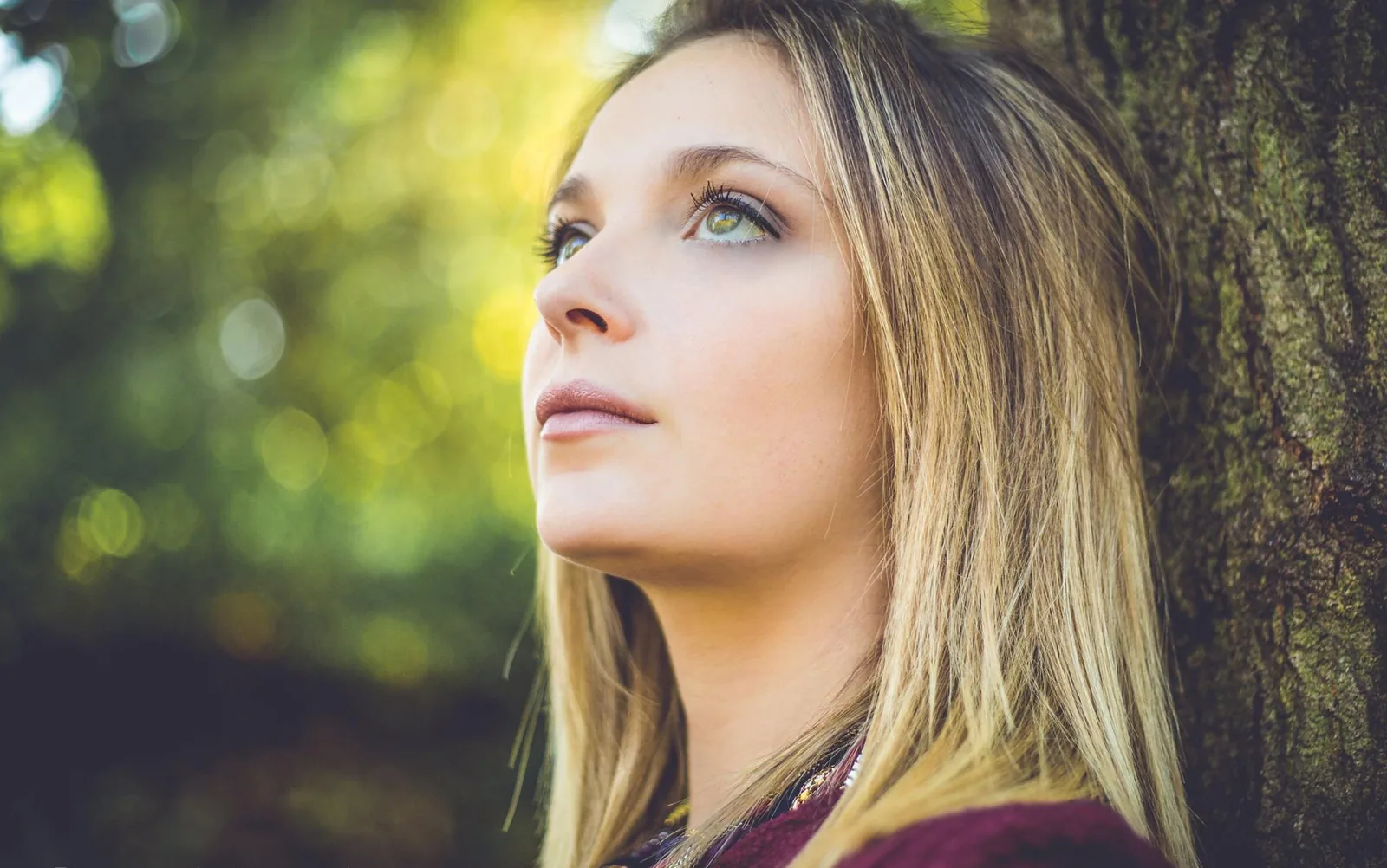 Regard levé vers le ciel, adossée à un arbre