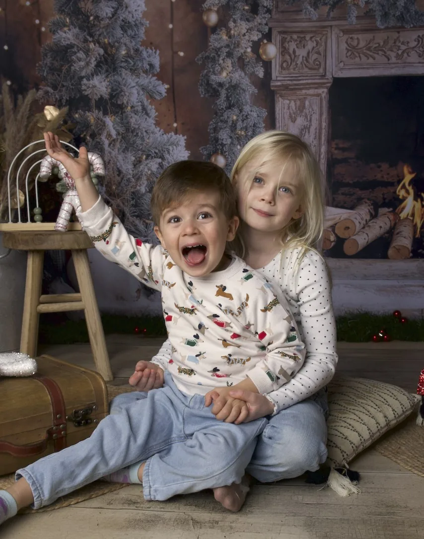 Un petit garçon crie de joie dans les bras de sa grande sœur, décor de Noël