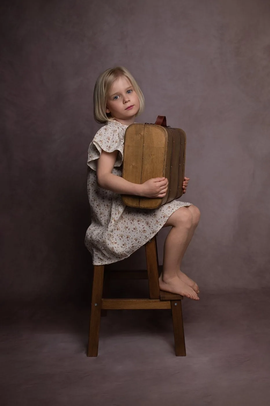 Fillette assise sur un tabouret, serrant une valise