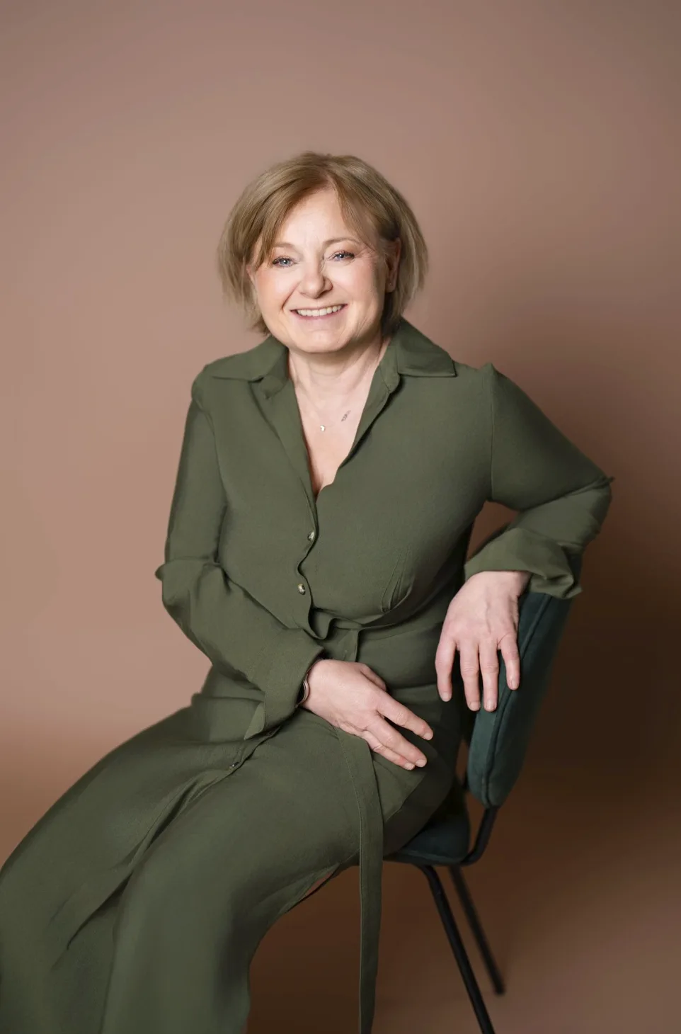 Femme souriante assise sur une chaise, robe chemise verte
