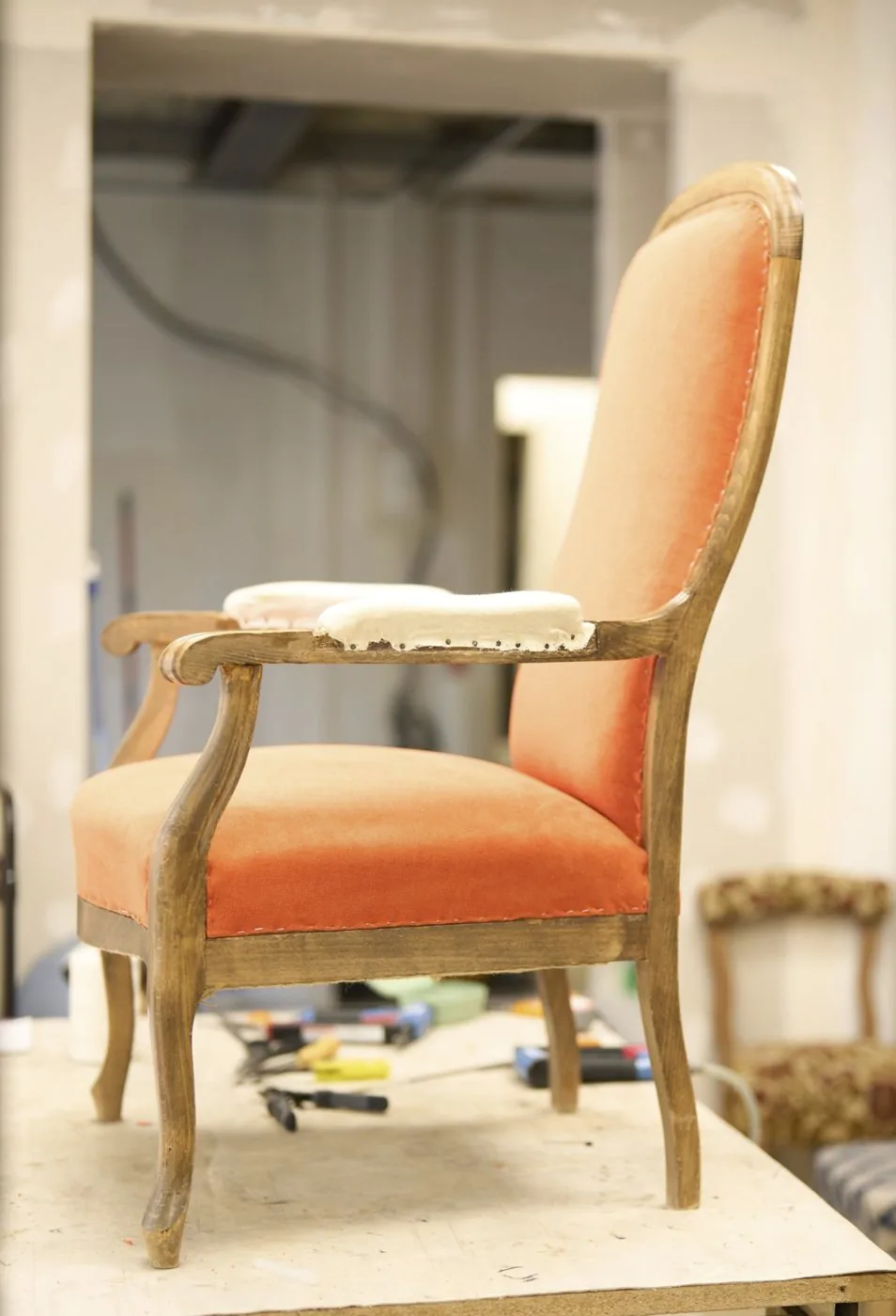 Fauteuil en velours orange en cours de réfection sur l'établi d'un tapissier